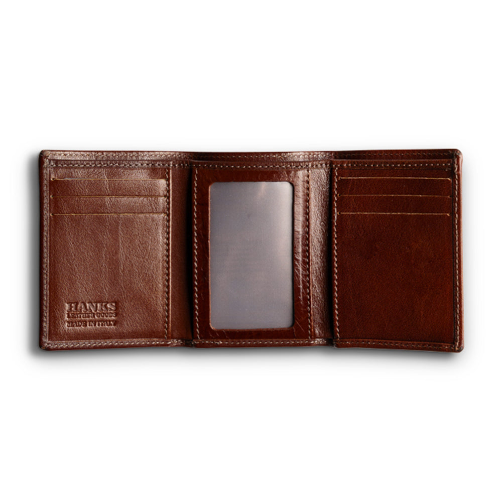 The Garda Italian Trifold with ID Window by Hanks Belts showcases Tuscan craftsmanship in dark brown leather, featuring multiple card slots and a clear ID holder. Empty interiors highlight its exquisite stitching, with &quot;Hanks Leather Goods&quot; elegantly embossed on the left side.