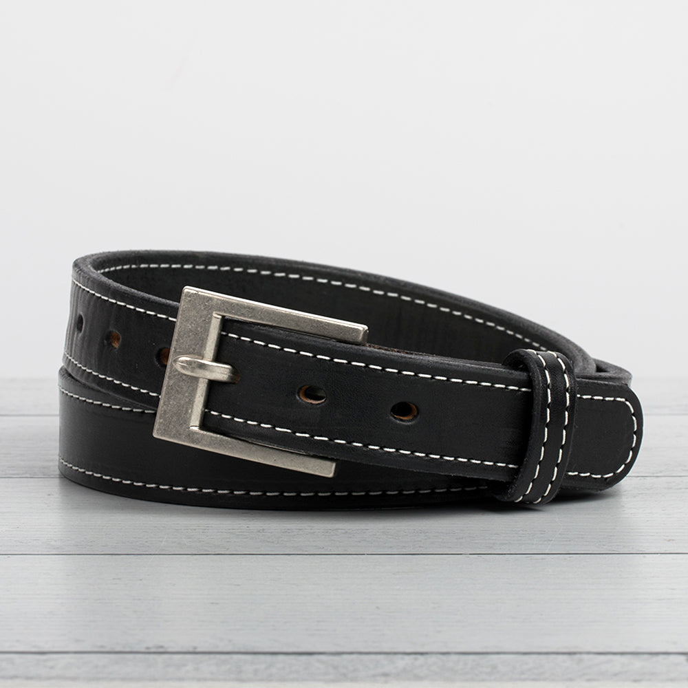 Hanks Belts&#39; Bonnie Belt - 1.25&quot;, made of full-grain leather with white stitching and a metallic buckle, is beautifully coiled on a light wooden surface against a plain white background.