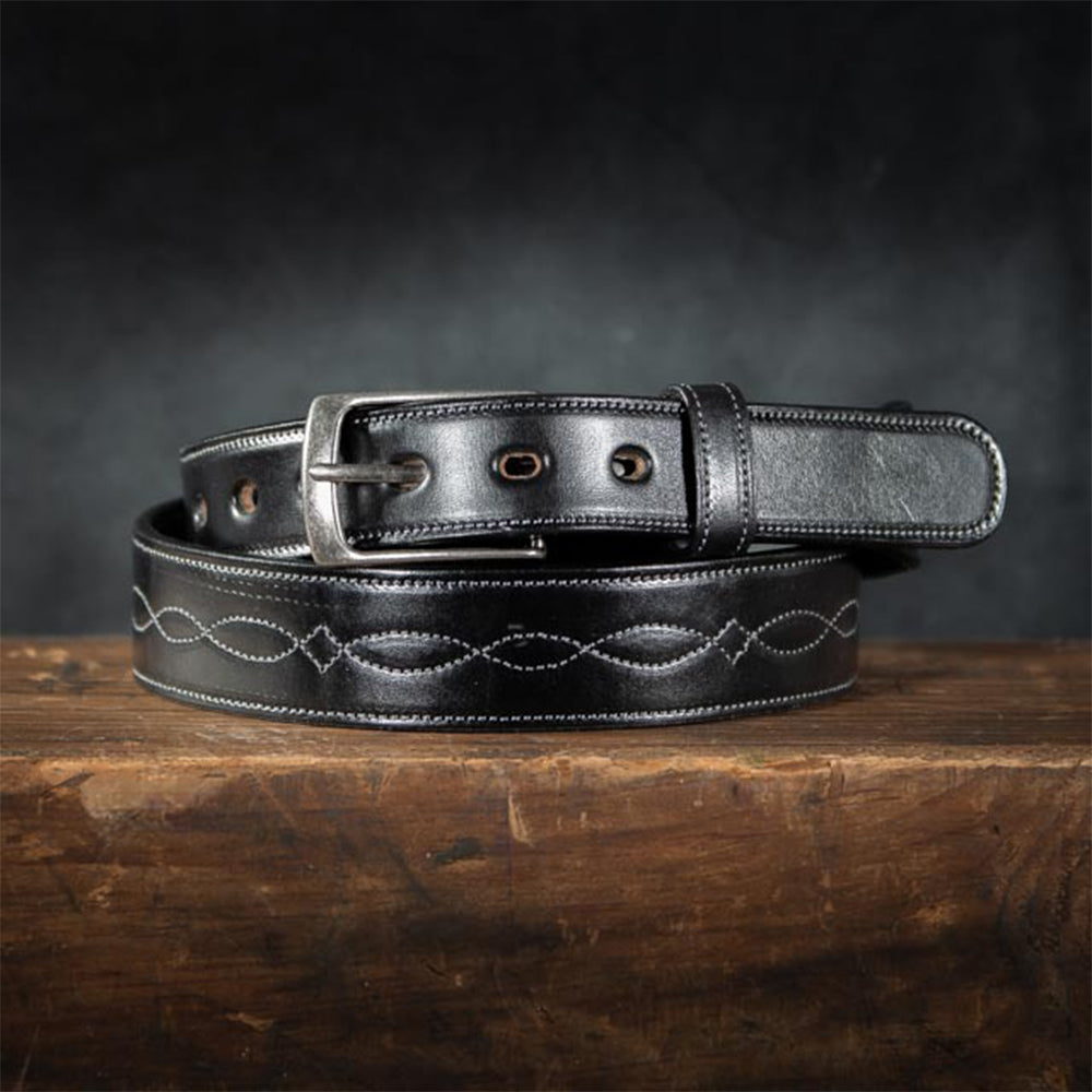 A 1.5&quot; black Teton belt by Hanks Belts, made of premium leather with a silver buckle and decorative stitching, is neatly coiled on a wooden surface against a subtly textured dark background.