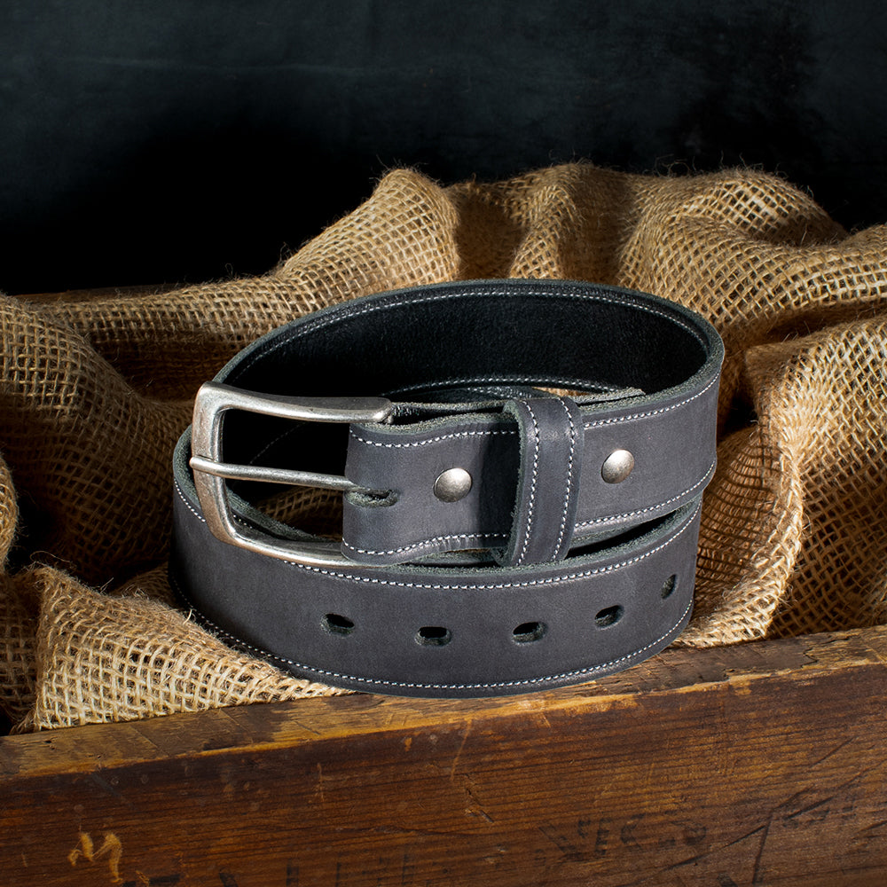 The Suede Belt - 1.5&quot; by Hanks Belts, made in the USA, is coiled on burlap. The rustic wooden backdrop contrasts beautifully with the suede&#39;s sleek texture and silver buckle.