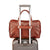 The Getaway Duffel With Luggage Sleeve by Hanks Belts, crafted in brown Italian leather, is stylishly affixed to the extended handle of a silver hard-shell suitcase. This combination captures the essence of luxury travel against a clean, minimalist backdrop, highlighting its carry-on-friendly design.