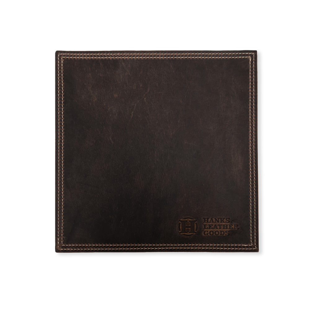 A square piece of luxurious dark brown bison leather showcasing visible stitching along its edges, this mouse pad is elegantly embossed in the bottom right corner with &quot;Hanks Belts&quot; and a circular logo featuring the letter &quot;H&quot;. Handmade in the USA, it&#39;s a refined accessory that enhances any workspace.