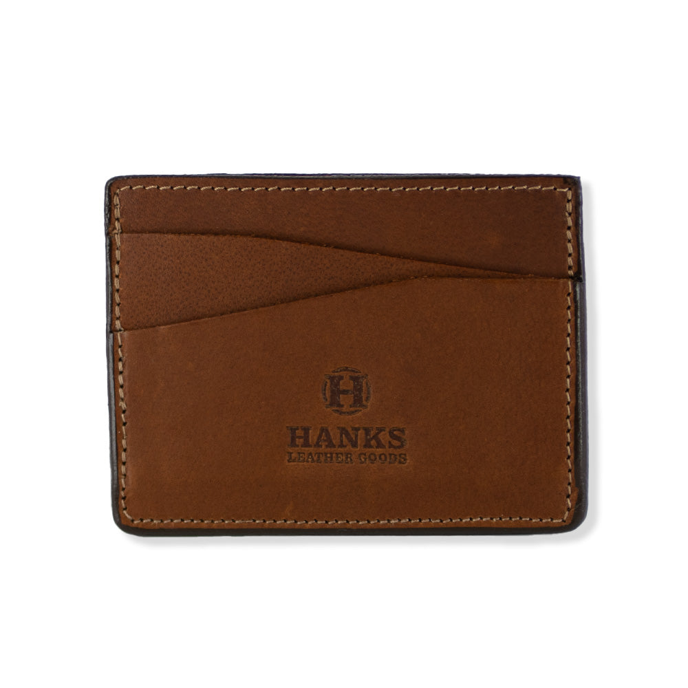 Introducing the Cumberland Bison Card Holder by Hanks Belts: a peanut brown leather card holder crafted from durable Bison Leather, showcasing the brand name &quot;Hanks Leather Goods&quot; with an embossed logo on the front. This ultra-thin, lightweight wallet is made in the USA and features two slanted card slots along with visible stitching along the edges for a timeless look.