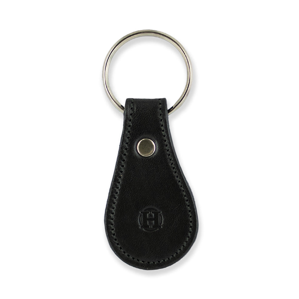 The Bell-Shaped Leather Keychain by Hanks Belts is crafted from premium black full-grain leather, designed with a teardrop contour and fitted with a durable metal keyring. Made in the USA, this keychain features a circular embossed logo near the bottom and a metal rivet at the top to securely fasten the leather loop. The visible stitching around the edges adds an extra touch of craftsmanship.