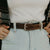 A person wearing light blue jeans with hands in pockets and a women's western belt from Hanks Belts, featuring the ornate floral buckle set of the Willow Belt - 1.25". The ensemble also includes a white shirt partially covered by a plaid jacket, highlighting both style and durability.