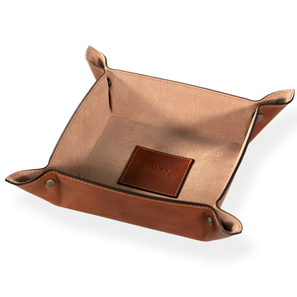 The Italian Large Valet Tray by Hanks Belts is a square, travel-ready accessory crafted from brown full-grain leather. It features snap buttons at each corner that reveal a soft tan interior. The base highlights an embossed logo on a small leather patch. Set against a plain white background, it&#39;s perfect for keeping your essentials organized.