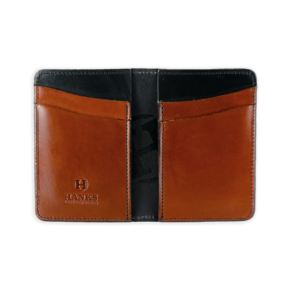 The Superior Front Pocket Bifold by Hanks Belts is a USA-made wallet crafted from premium harness leather, featuring an embossed &quot;HANKS&quot; logo on the bottom left with two brown pockets and a black interior.