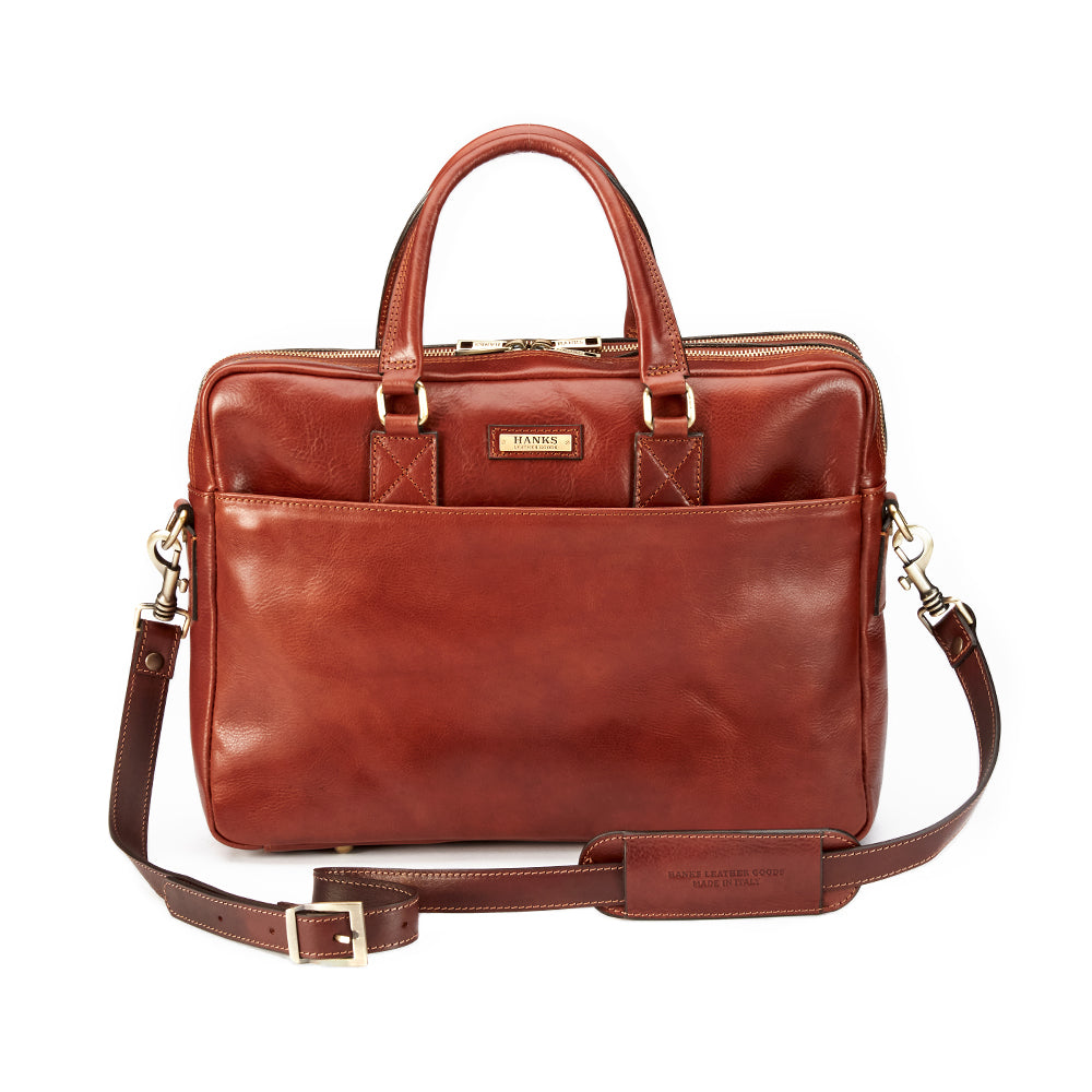 The Practical Laptop Bag from Hanks Belts, crafted from premium Italian leather in a brown finish, merges luxury with functionality. It comes with two handles, a detachable shoulder strap, a front pocket highlighted by visible stitching, and showcases a gold brand logo on the front.