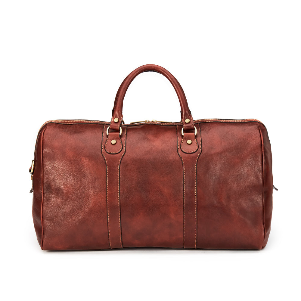 Introducing the Wanderer Duffel by Hanks, a large handcrafted Italian bag made from exquisite brown leather. It features the back with dual handles and elegant gold-tone hardware. The smooth texture and zippered top closure exude luxury, all beautifully showcased against a plain white background.