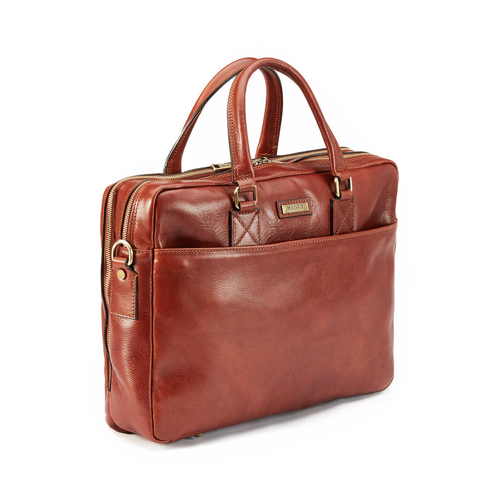 The Practical Laptop Bag by Hanks Belts is a chic carryall made from high-quality Italian leather. It features dual handles, a front pocket, and boasts a structured design with a zipper closure. The gold-tone hardware perfectly blends luxury with functionality, making it ideal for professional use.