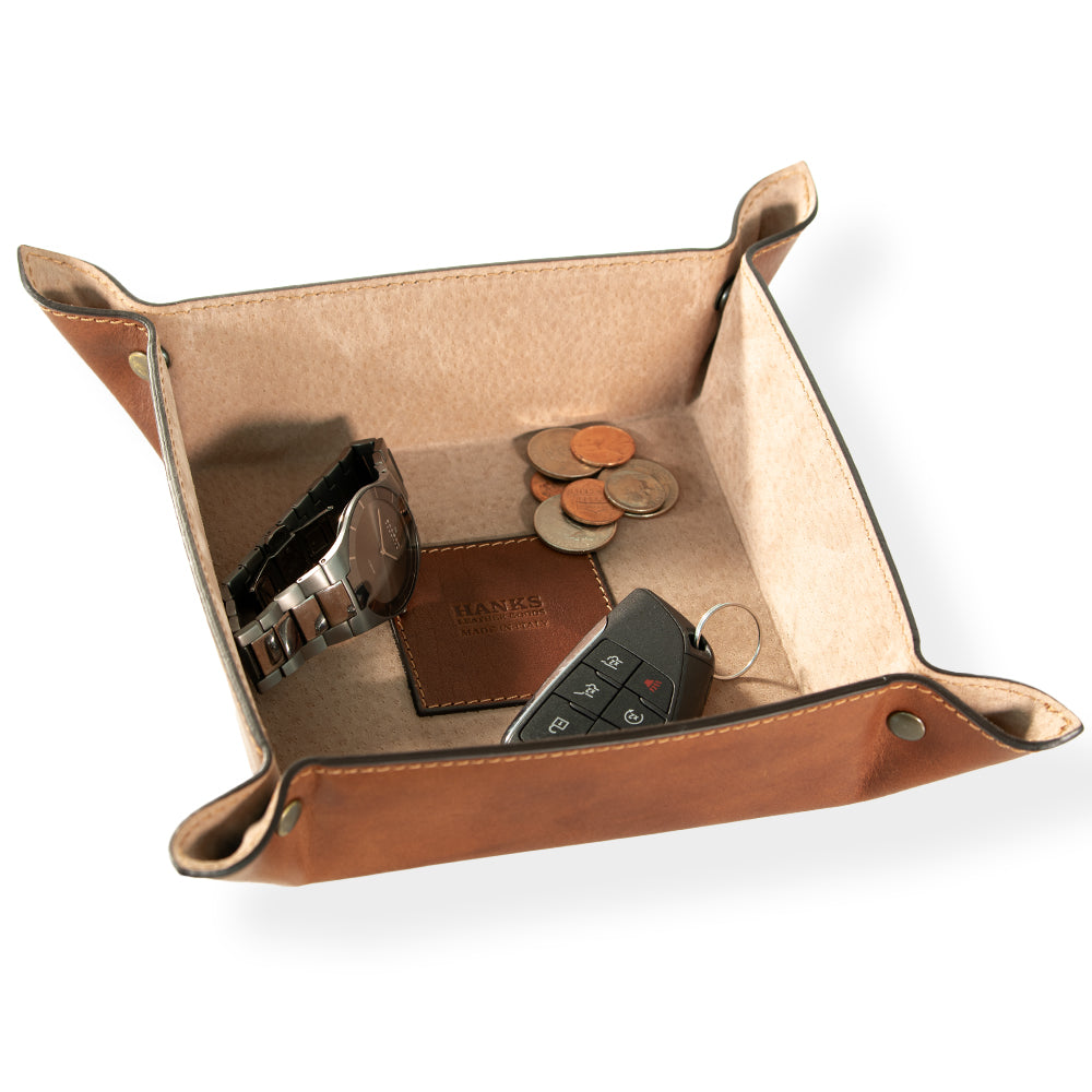 The Italian Large Valet Tray by Hanks Belts is crafted from full-grain leather and is perfect for travel. It holds a watch, coins, a car key, and a leather accessory, featuring reinforced corners and metal snaps to keep these essentials neatly stored.