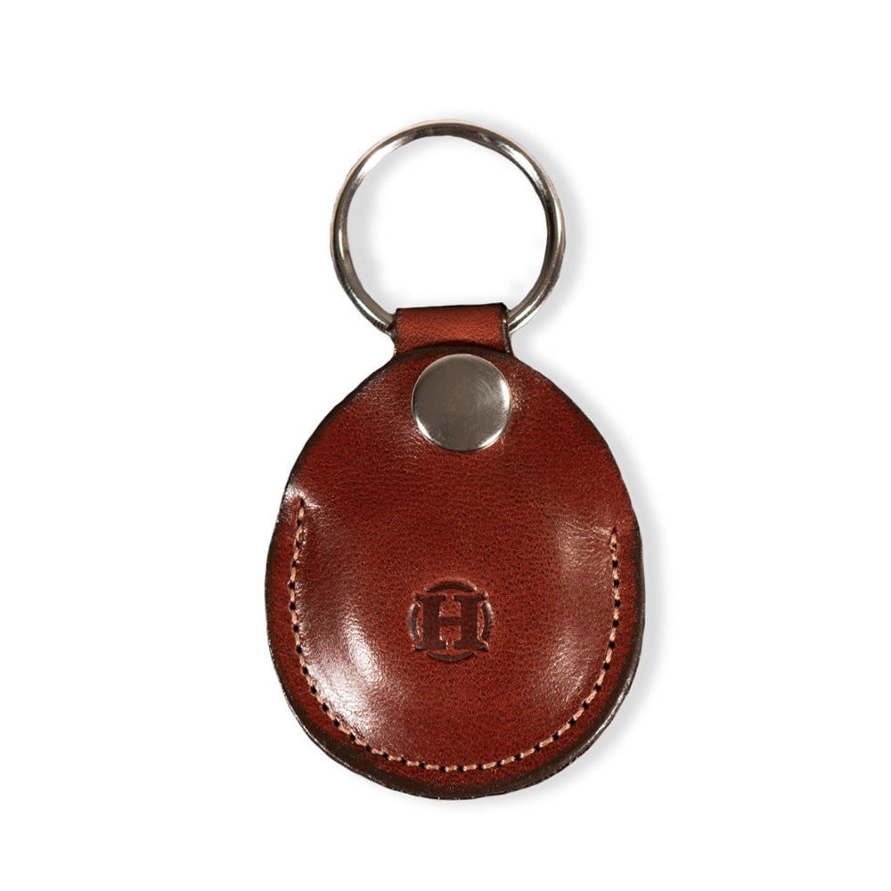 The Circular Tag Holder from Hanks Belts is an oak leather keychain made from USA-tanned full-grain hide. It features a circular metal ring, stitched border, and a small embossed &quot;H&quot; at the center, making it an ideal AirTag leather holder option.