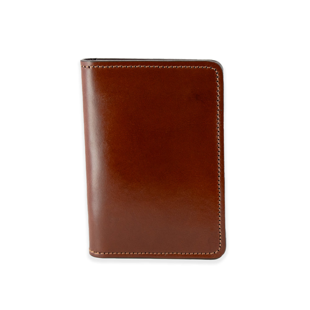 The Superior Front Pocket Bifold wallet by Hanks Belts, crafted from premium USA-tanned harness leather, is shown closed with a smooth finish and beige stitching along the edges. Its vertical orientation is captured against a plain white background.