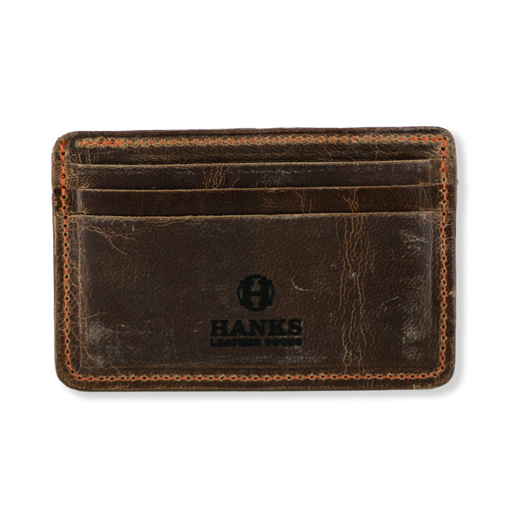 The Hamlin Card Holder with ID Window by Hanks Belts is a brown, worn-looking accessory made from durable Steerhide leather. It features three slots on the front and stitching around the edges. Proudly made in the USA, it showcases the &quot;HANKS&quot; logo in black at the bottom center.