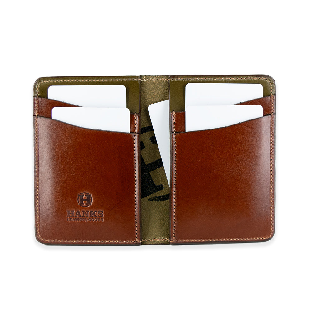 The Superior Front Pocket Bifold by Hanks Belts is an open brown handcrafted wallet made from premium USA harness leather. It has four card slots, each holding a white card, a stitched design, &quot;HANKS&quot; embossed on the lower left side, and an olive green interior lining.