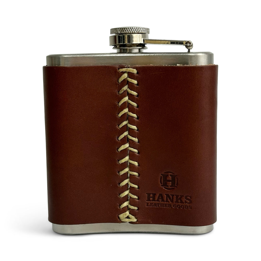 The Hanks Belts Leather Covered Flask, crafted from stainless steel and wrapped in oak-colored USA tanned leather with a screw-on cap that includes a hinged arm, is shown standing upright against a white background.