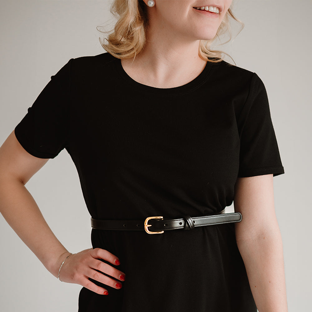 A person in a black dress with the Hanks Dixie Belt in Black - .75&quot; smiles slightly. They have light hair and wear earrings, accessorized with a versatile bracelet. The plain background emphasizes the outfit.