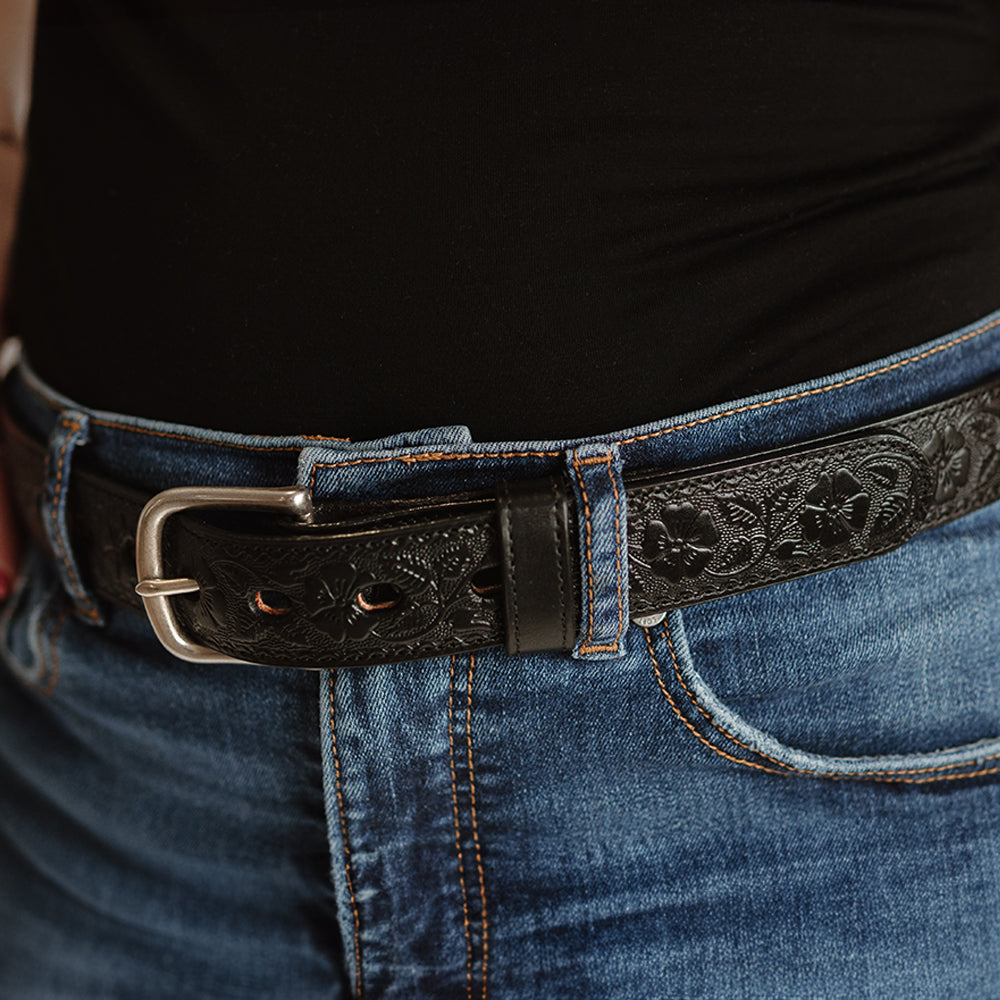 A person in USA-made blue jeans wears a Hanks Belts Floral Belt - 1.25&quot;, intricately patterned and crafted from full-grain leather with a visible metal buckle, paired with a sleek black top.